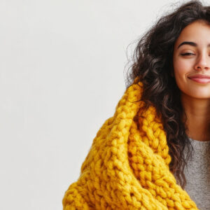 Lächelnde Frau mit geschlossenen Augen in gelber Kuscheldecke - Fortbildungsreihe Resilienz und Achtsamkeit für Fachkräfte
