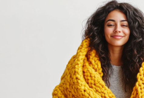 Lächelnde Frau mit geschlossenen Augen in gelber Kuscheldecke - Fortbildungsreihe Resilienz und Achtsamkeit für Fachkräfte