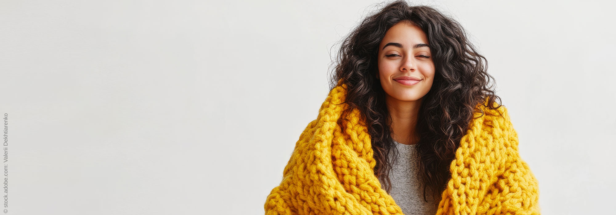 Lächelnde Frau mit geschlossenen Augen in gelber Kuscheldecke - Fortbildungsreihe Resilienz und Achtsamkeit für Fachkräfte