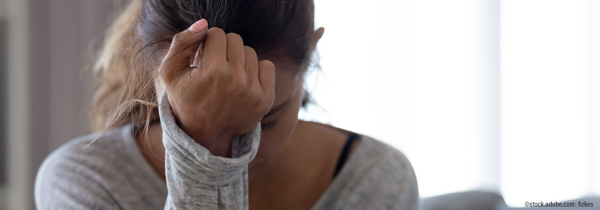 Frau mit Pferdeschwanz hält erschöpft Hand an Kopf und zeigt Überforderung - Impulsvortrag Belastungsempfinden