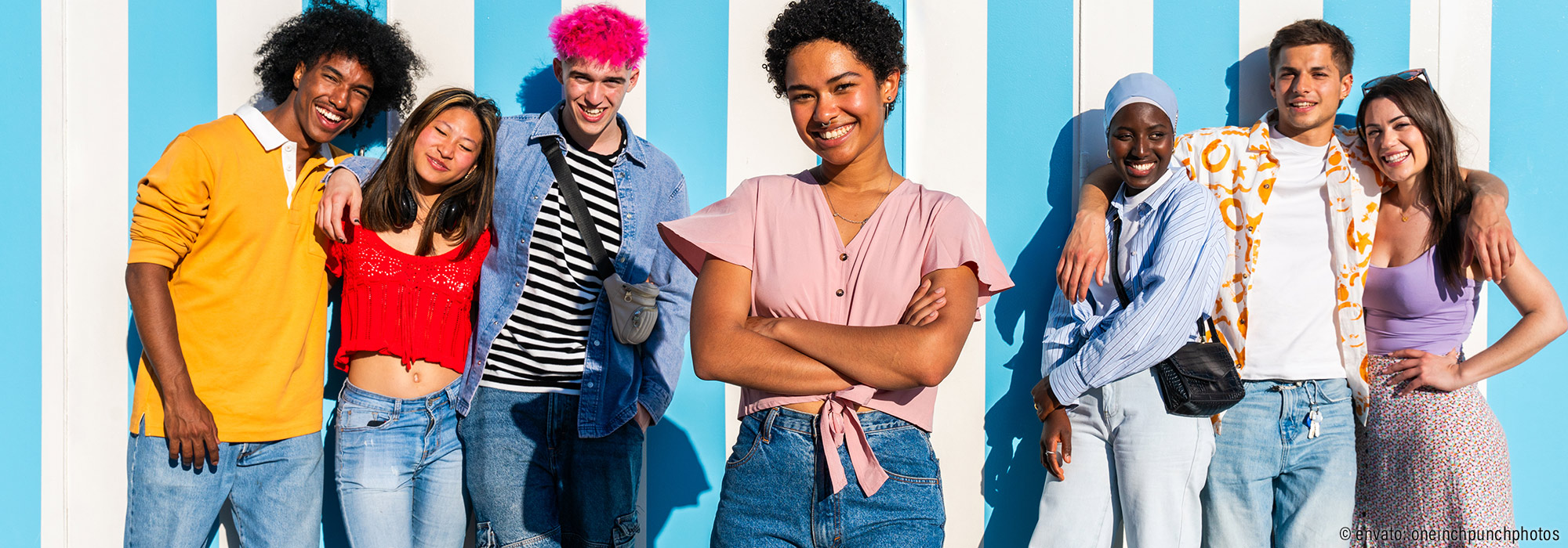 Diverse Gruppe junger Menschen in bunter Kleidung vor blau-weißer Wand - Fortbildungsreihe Schulbegleitung Lebenshilfe Alfeld