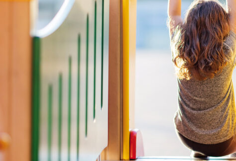 Kind von hinten sitzt auf Spielplatzrutsche und blickt hinaus - NEAS Impuls Neues Kind und ich weiß kaum was