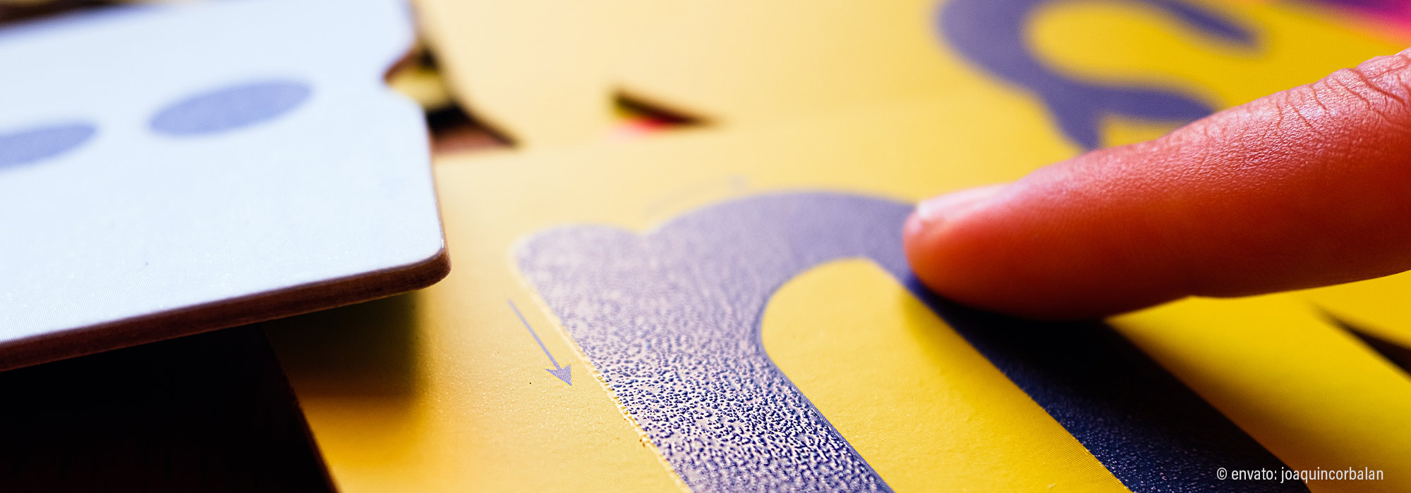 Nahaufnahme Finger zeigt auf taktile Kommunikationskarte mit farbigen Symbolen und Braille - Fachmodul für unterstützte Kommunikation Autismus Spektrum